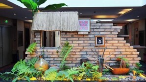A lobby with a brick wall, a hanging plant, a thatched roof, and a stone fireplace. - Mijng Qiyuan Minority Theme Hotel (Mojiang)