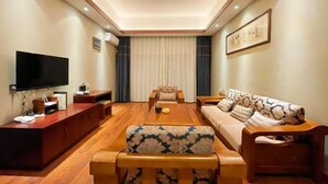 A modern living room with a flat-screen TV, wooden furniture, a sofa with a floral pattern, and a framed artwork on the wall. - Mijng Qiyuan Minority Theme Hotel (Mojiang)