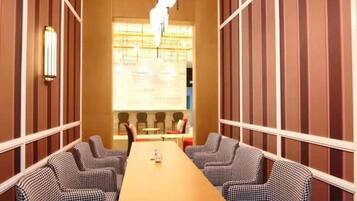 A conference room with a long table and four chairs, a large window with blinds, and a wall-mounted light fixture.
