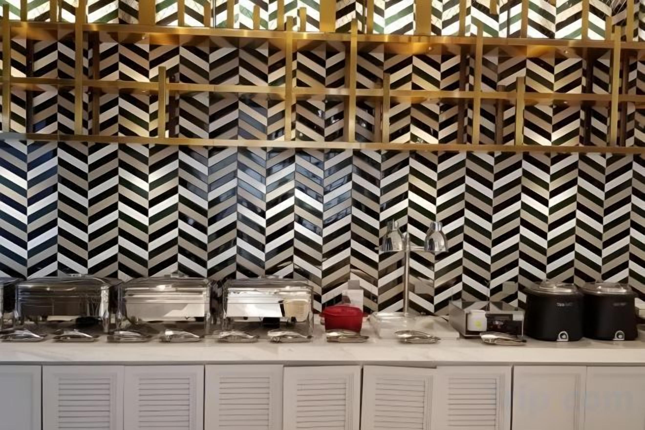 A buffet setup with various food containers and a patterned wall in the background.