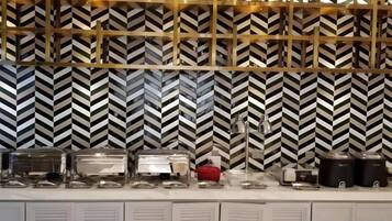 A buffet setup with various food containers and a patterned wall in the background.