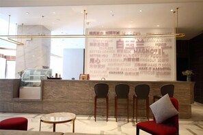 A reception area with a marble counter, four chairs, a red sofa, and a glass coffee table. - Magnotel Hotel (Nanjing Lishui Development Zone Baota North Road) (Nanjing)