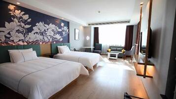 A hotel room with two beds, a sofa, a TV, and a large floral mural on the wall.