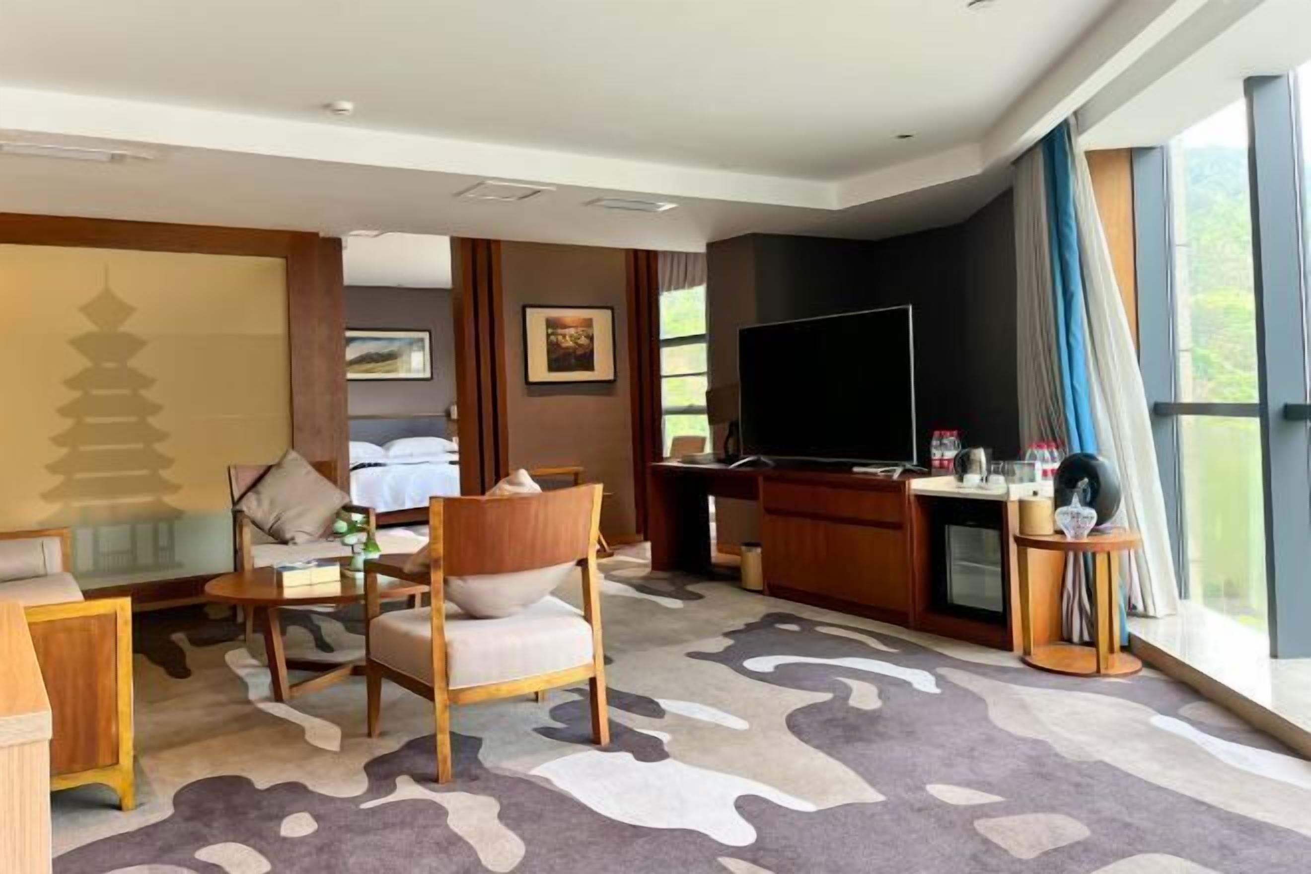 A hotel room with a bed, a desk with a computer, a television, and a large window.