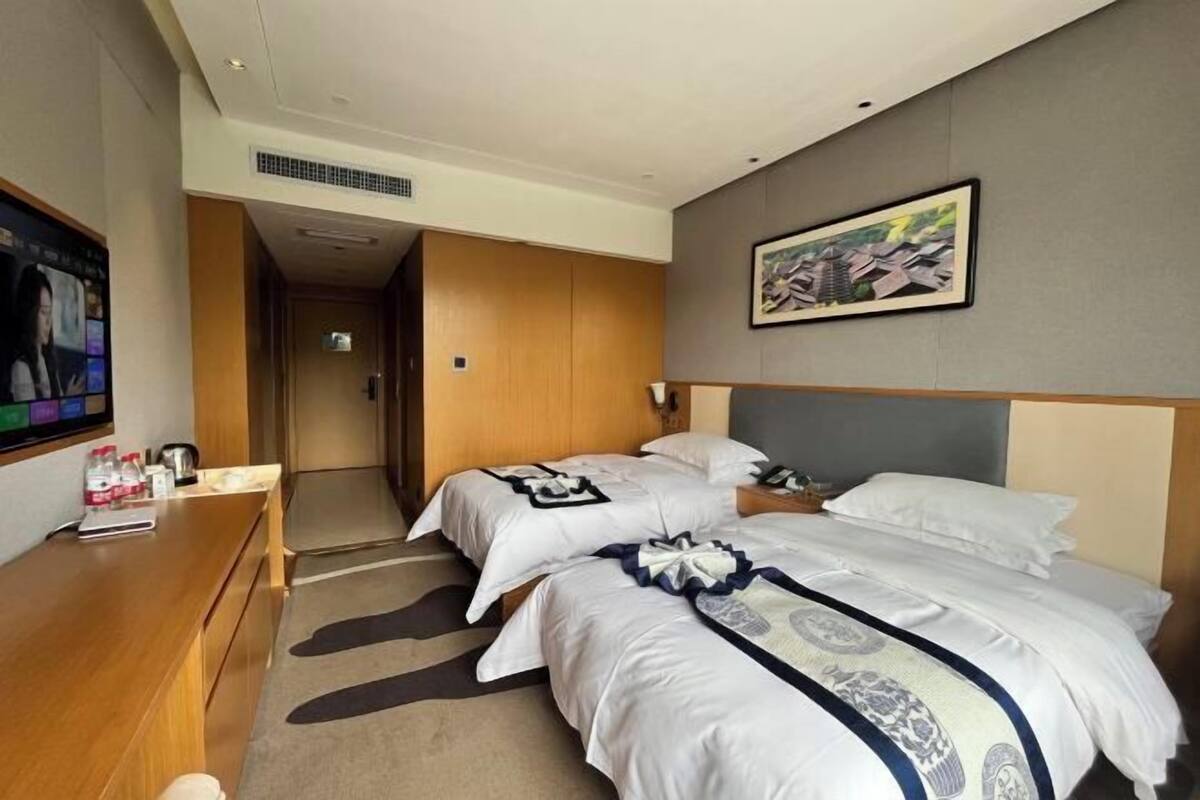 Ein Hotelzimmer mit zwei Betten, einem Schreibtisch, einem Fernseher und einem Bild an der Wand.