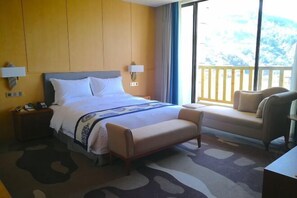 Quarto de hotel com cama, mesas de cabeceira, um banco, uma cadeira e varanda com vista.