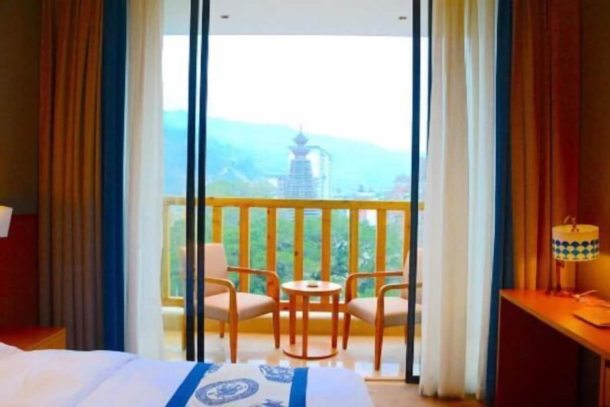 Ein Hotelzimmer mit Bett, einem kleinen Tisch mit Stühlen und Blick auf einen Tempel vom Balkon aus.