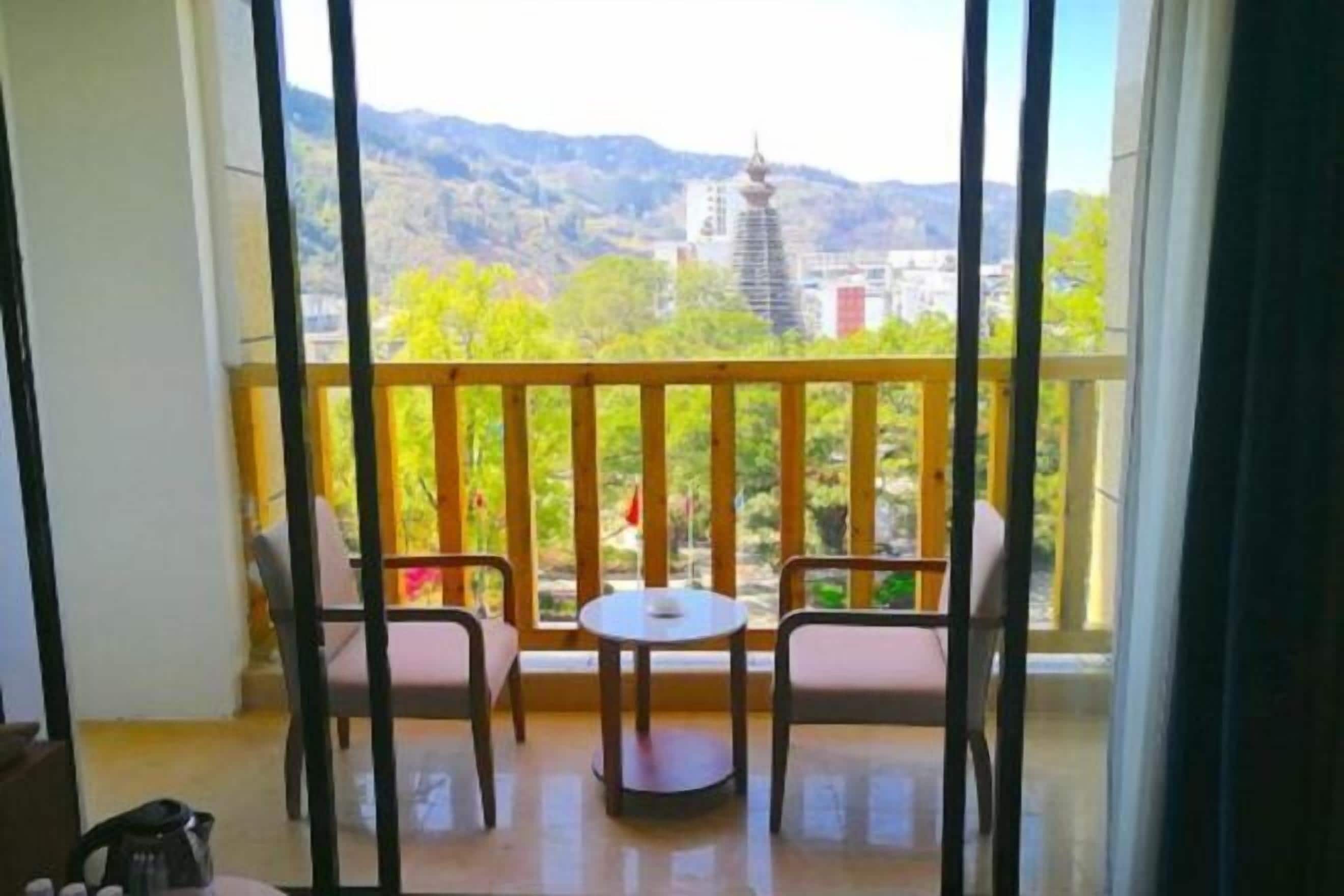 A balcony with two chairs and a small table, offering a view of a mountain and buildings.