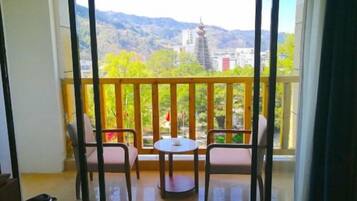 A balcony with two chairs and a small table, offering a view of a mountain and buildings.