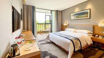 A hotel room with a bed, a desk with a kettle, a chair, a balcony with a view, and a painting on the wall.