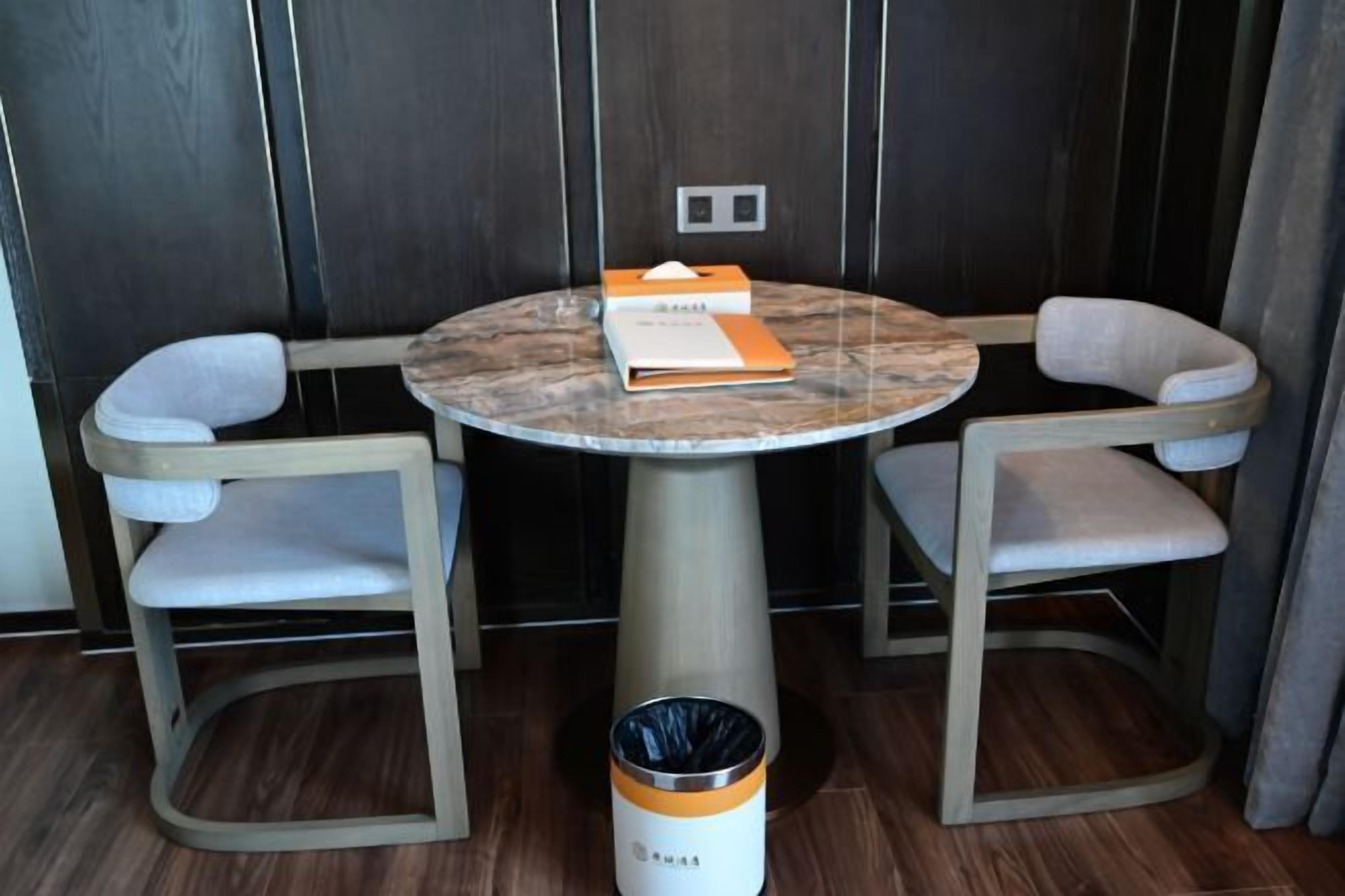 A round table with two chairs, a trash bin, and a wall-mounted light switch.