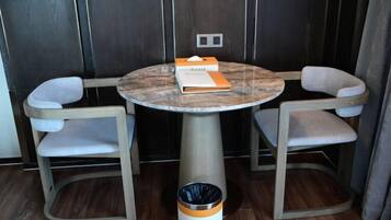 A round table with two chairs, a trash bin, and a wall-mounted light switch.