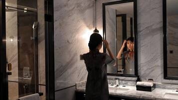 A modern bathroom with a large mirror, marble walls, and a glass shower enclosure.