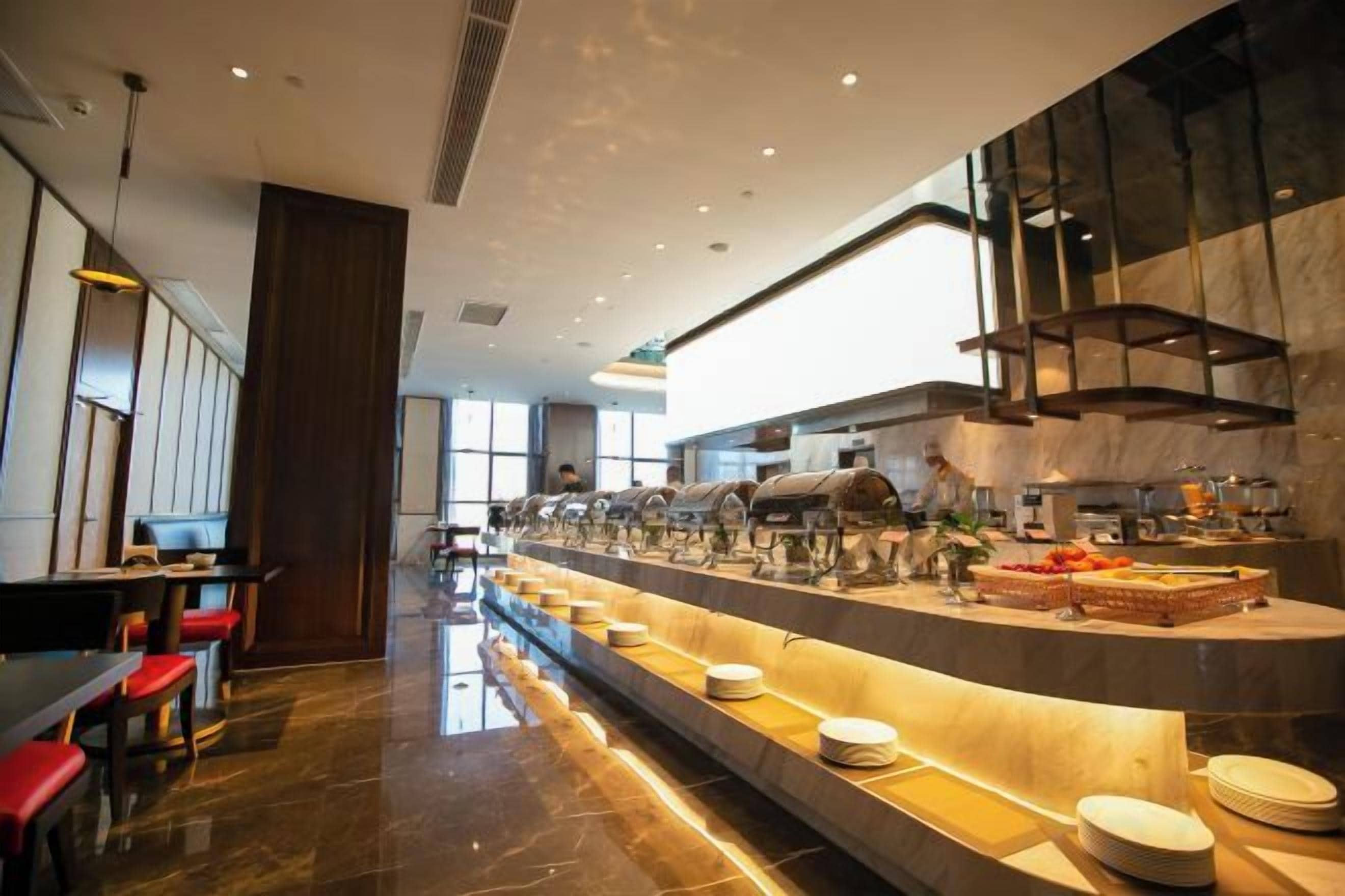A modern hotel lobby with a long reception counter, seating area, and a large window providing natural light.