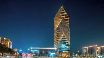 A high-rise building with a unique triangular design, surrounded by illuminated streets and other buildings.