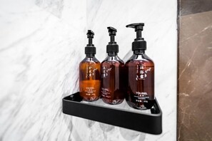 Three toiletry bottles on a black shelf against a marble wall. - Gangcheng Hotel (Zhoushan)