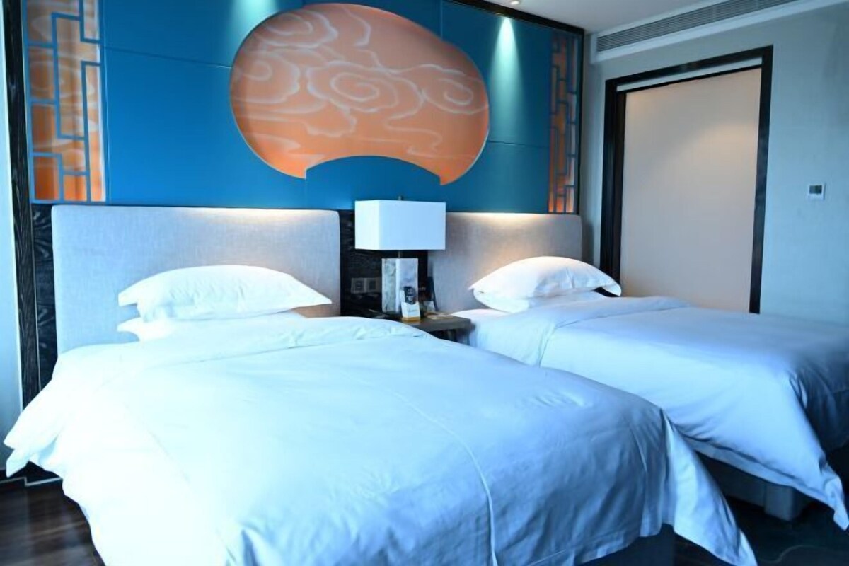 A hotel room with two beds, a large wall mural, and a nightstand with a lamp.