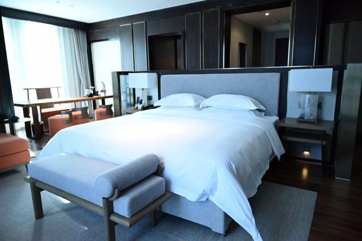 A modern hotel room with a large bed, a desk, and a seating area.