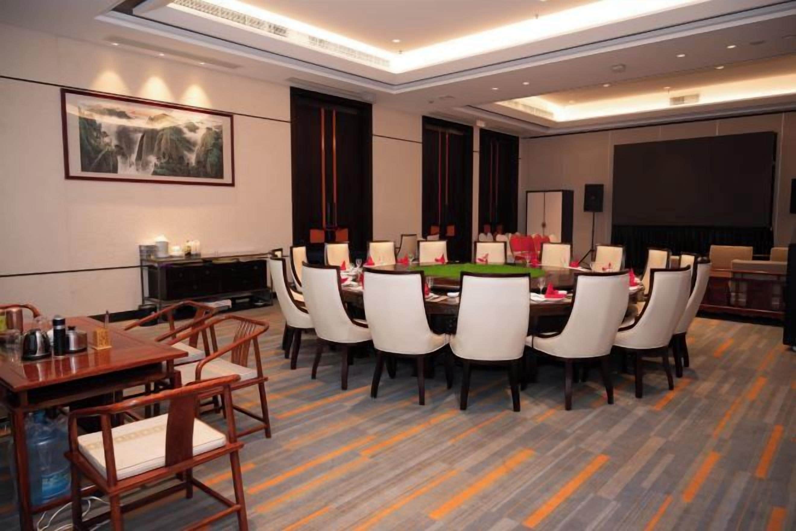 A hotel dining area with a round table, chairs, and a television screen.