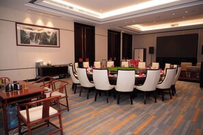 A hotel dining area with a round table, chairs, and a television screen. - Gangcheng Hotel (Zhoushan)
