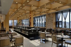 A spacious hotel dining area with a central bar, multiple seating arrangements, and large windows providing views. - Jiasheng Jinling Hotel (Nanjing)