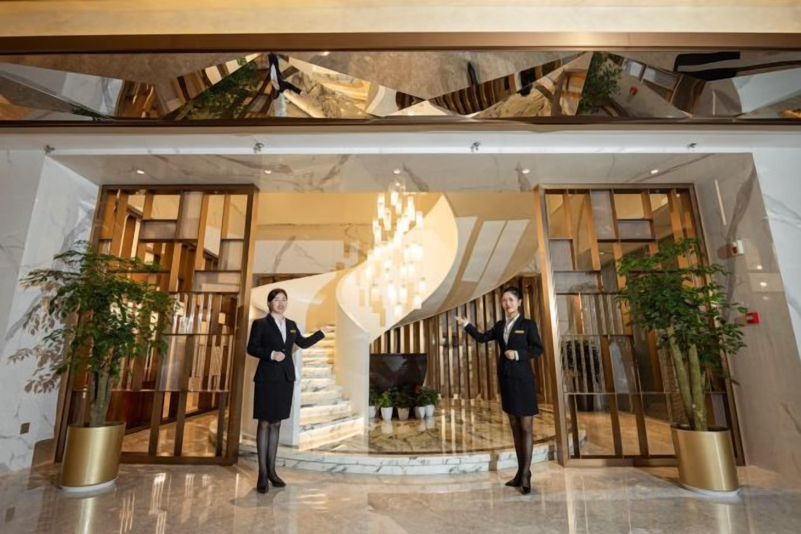 A lobby with a modern design, featuring a spiral staircase, large potted plants, and a chandelier.