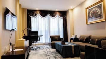 A hotel room with a piano, a sofa, a table, and a large window with curtains.