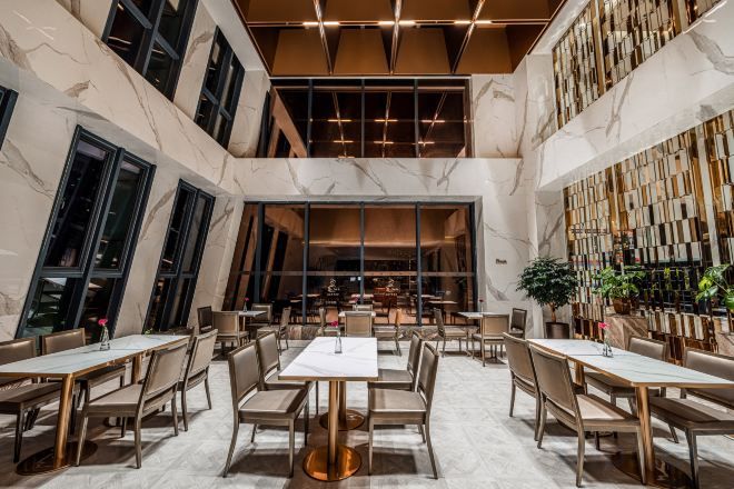 A spacious interior with high ceilings, marble flooring, and a central seating area with tables and chairs.