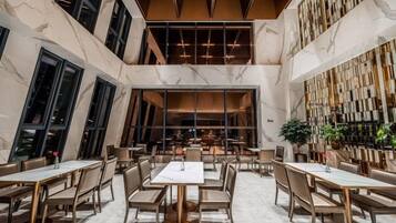 A spacious interior with high ceilings, marble flooring, and a central seating area with tables and chairs.