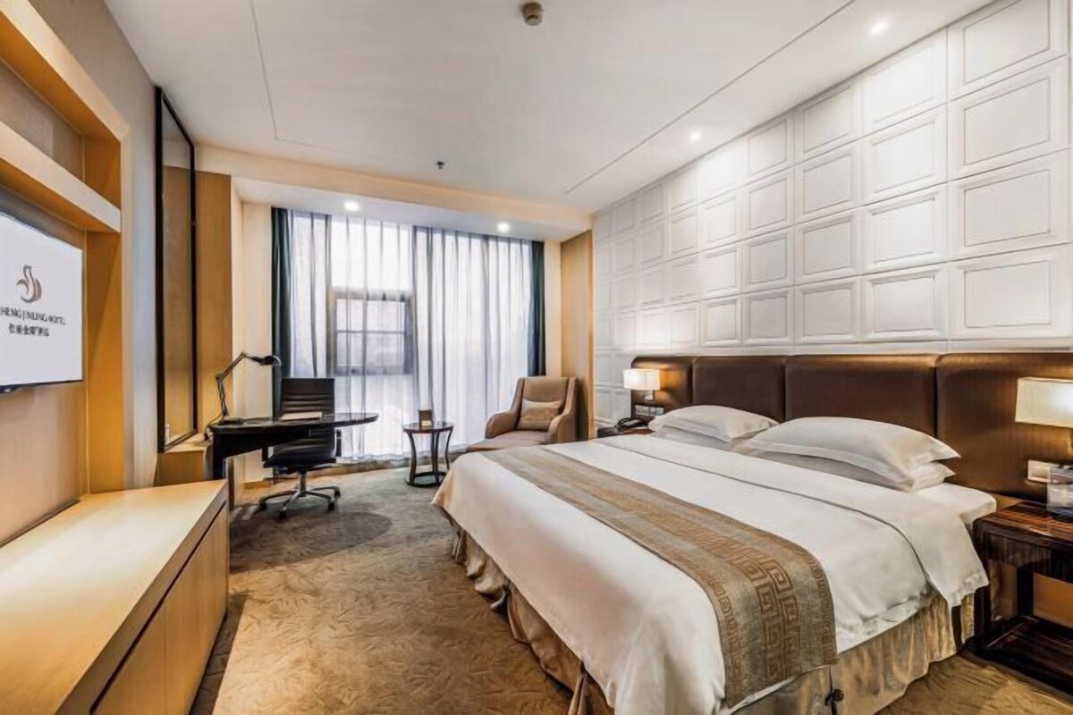 A hotel room with a large bed, a desk, a chair, and a TV screen.