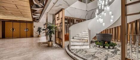 Un vestíbulo amplio con piso de mármol, una escalera curva y un candelabro moderno.