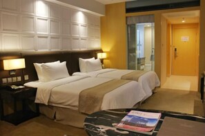 A hotel room with two beds, a nightstand with a lamp, a small table with a magazine, and a door leading to a bathroom. - Jiasheng Jinling Hotel (Nanjing)