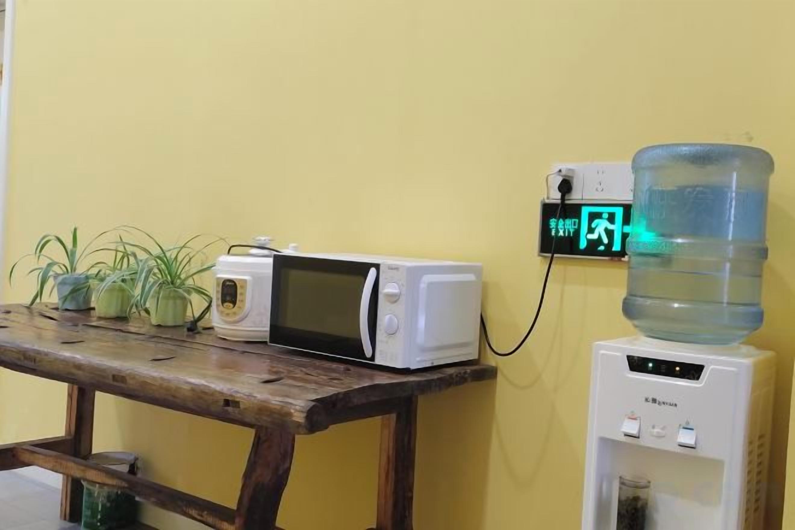 A microwave on a wooden table, a water dispenser, and a digital clock on a wall.