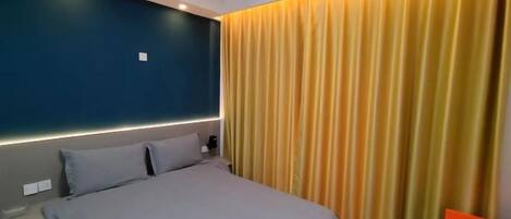 A hotel room with a bed, a nightstand, and a curtain.