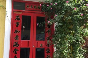 A red door with Chinese characters, a window, and a plant with pink flowers. - Anyang Hongmen Homestay (Normal College) (Anyang)