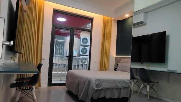 Ein Schlafzimmer mit Bett, Schreibtisch, Stuhl, Fernseher und einem Fenster mit Vorhängen.