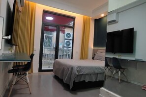 A bedroom with a bed, a desk, a chair, a TV, and a window with curtains.