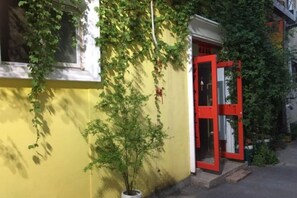 A yellow building with a red door, a potted plant, and a window with white trim. - Anyang Hongmen Homestay (Normal College) (Anyang)