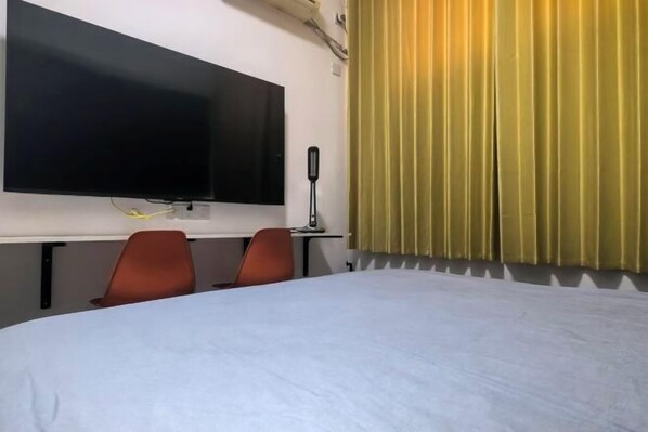 A hotel room with a large bed, a desk, a flat-screen TV, two chairs, and a window with yellow curtains. - Anyang Hongmen Homestay (Normal College) (Anyang)