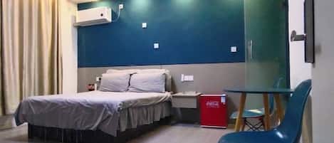 A hotel room with a bed, bedside table, chair, and a small table with a red object on it.