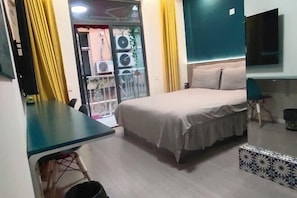 Makuuhuoneessa on sänky, työpöytä, tuoli, televisio ja parveke, jossa on keltaiset verhot.
