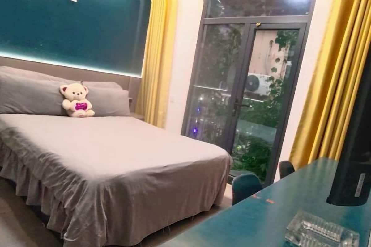 A bedroom with a bed, a teddy bear, a window with curtains, and a view of greenery outside.