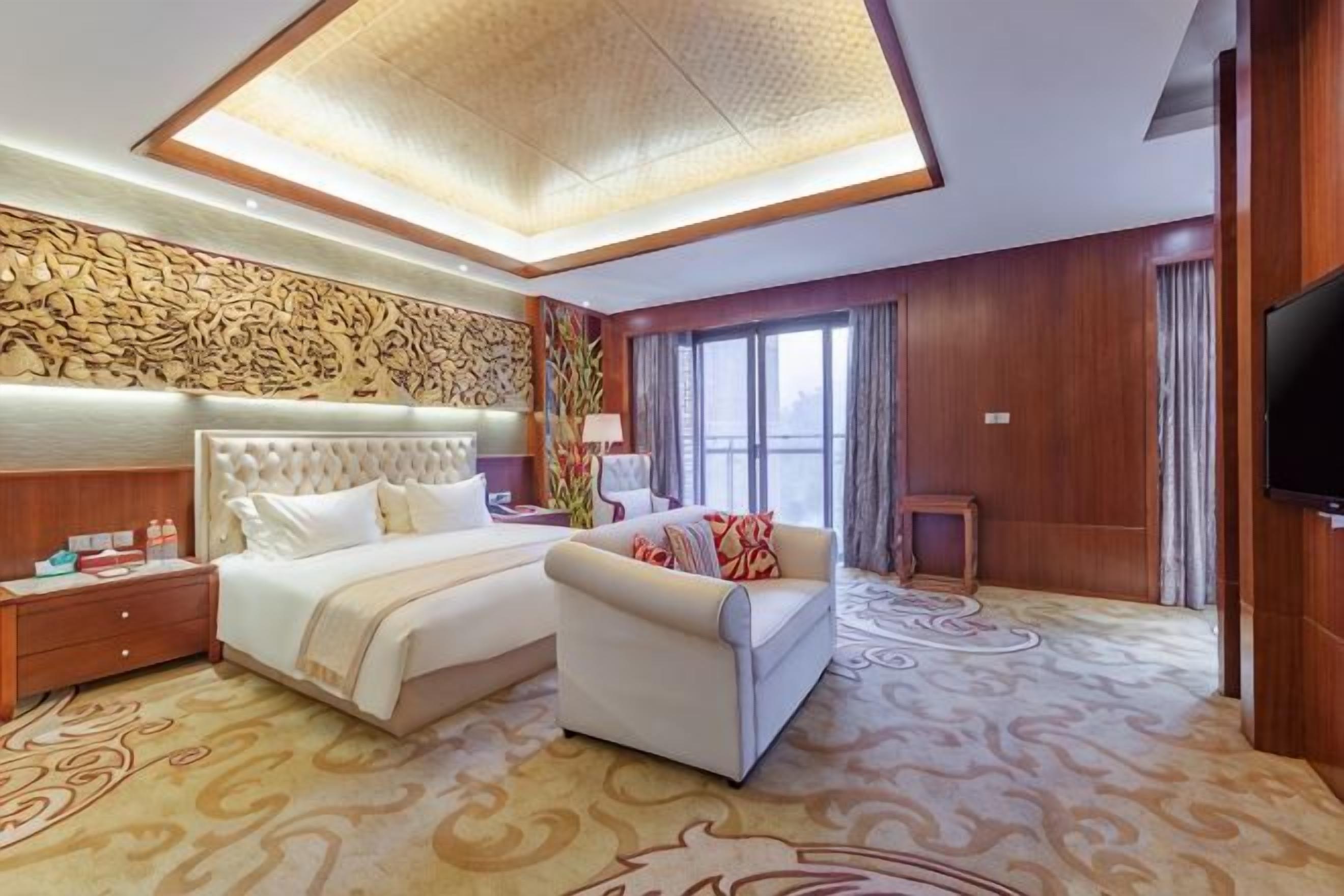 A hotel room with a large bed, a sofa, a TV, and a decorative wall.