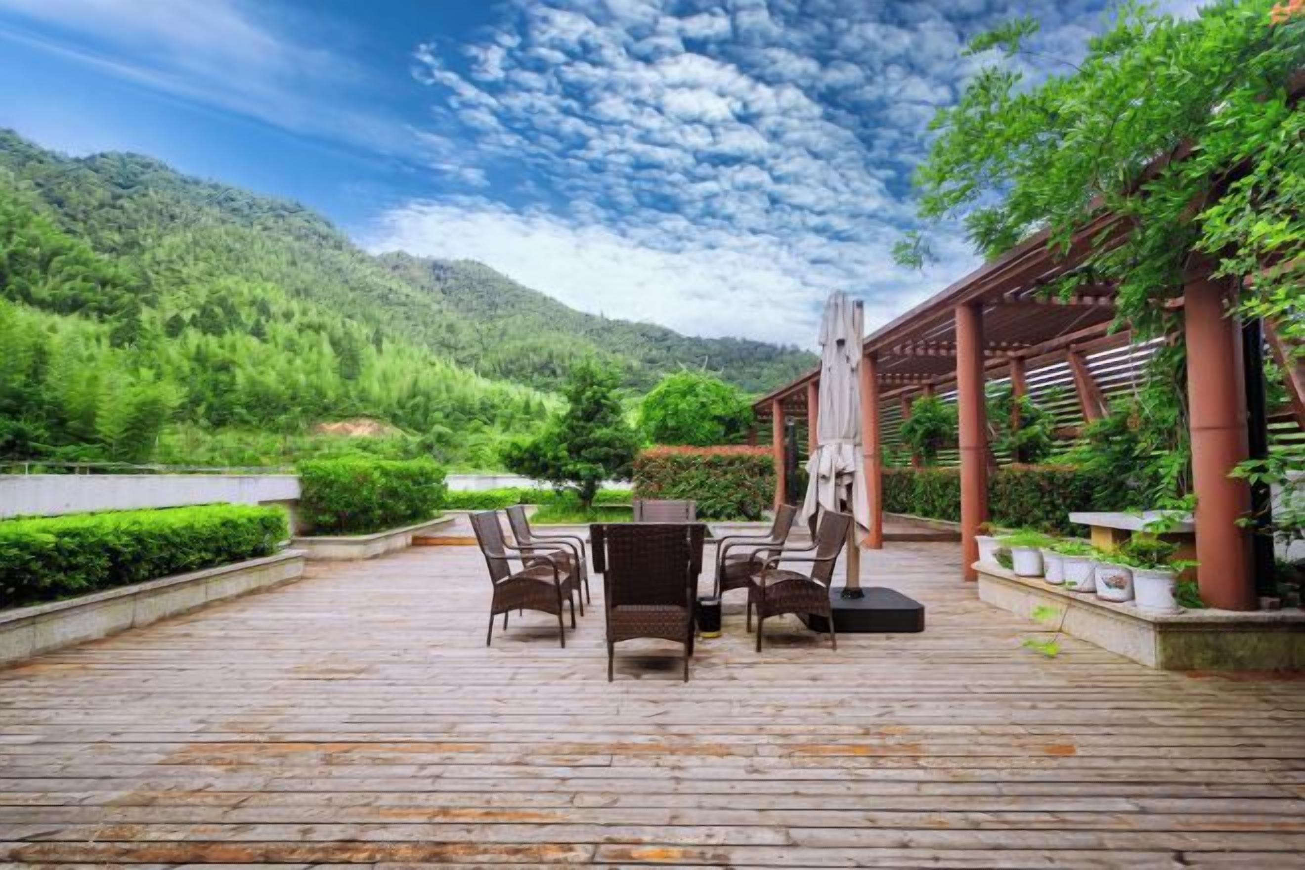 An outdoor patio with a table and chairs, surrounded by greenery and a mountain backdrop.