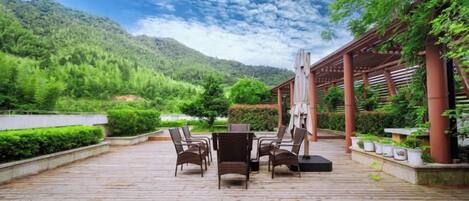 An outdoor patio with a table and chairs, surrounded by greenery and a mountain backdrop.