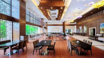 A spacious dining area with multiple tables and chairs, large windows, and a modern ceiling design.