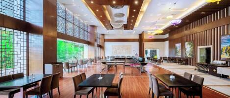 A spacious dining area with multiple tables and chairs, large windows, and a modern ceiling design.