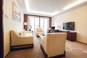 Habitación de hotel con sofá, sillón, escritorio, televisión y un ventanal grande.
