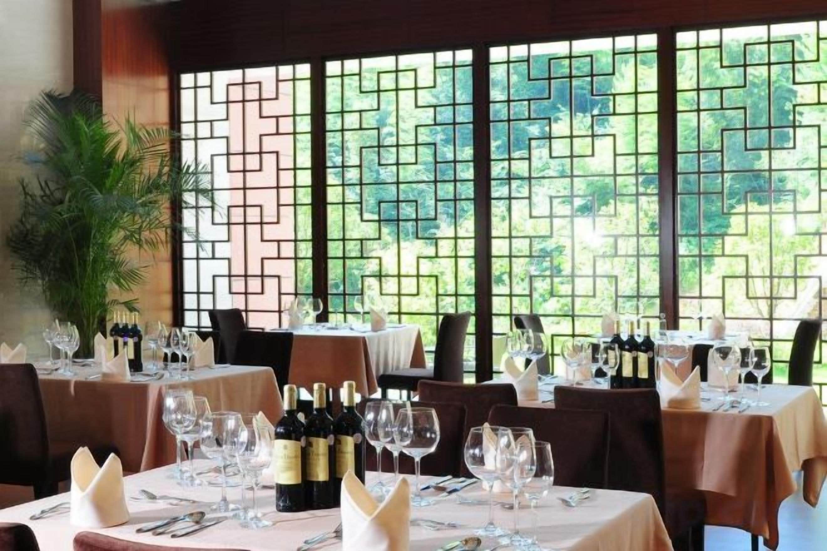 Un restaurante con mesas dispuestas para comer, con vista a través de una ventana de diseño geométrico.