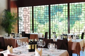 A restaurant with tables set for dining, featuring a view through a geometric patterned window. - Zhongxin Convention Center (Jinggangshan City)